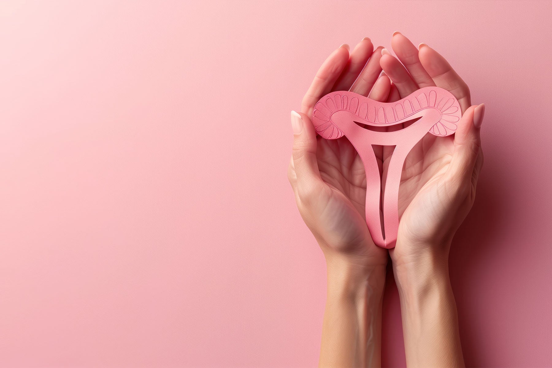 Woman hand holding uterus shape made from paper on pink background.