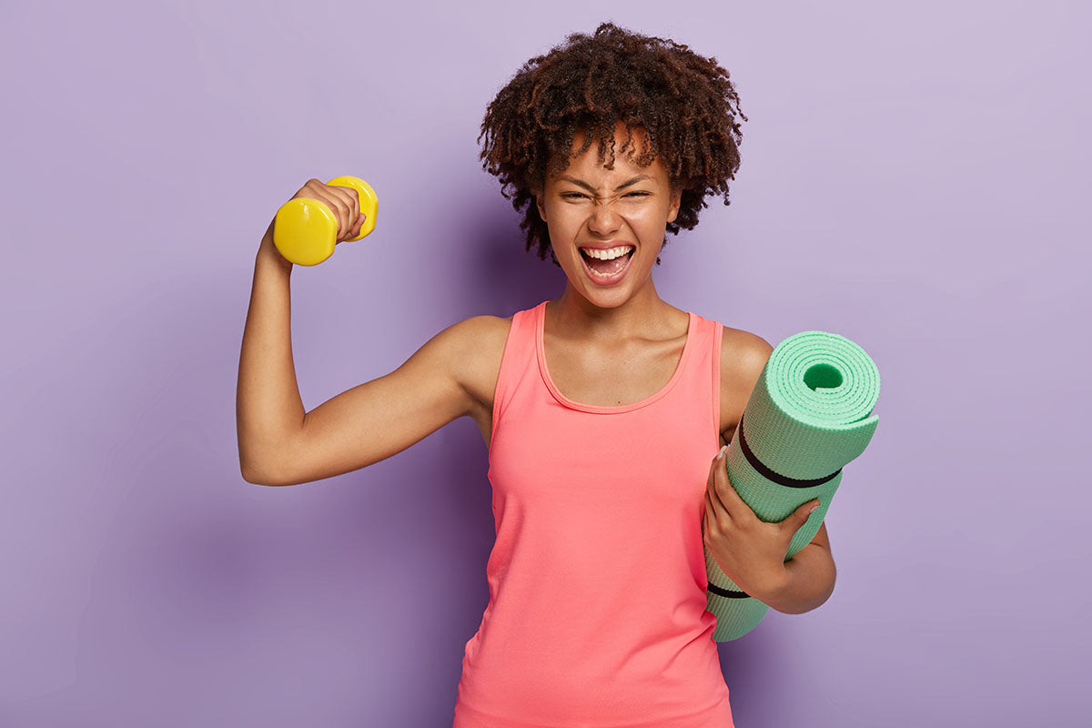 A woman holding a yoga mat with one arm and a dumbbell in the other