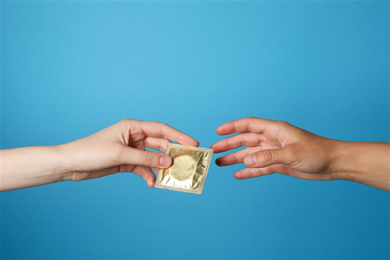 A condom is passed from hand to hand on a blue background.